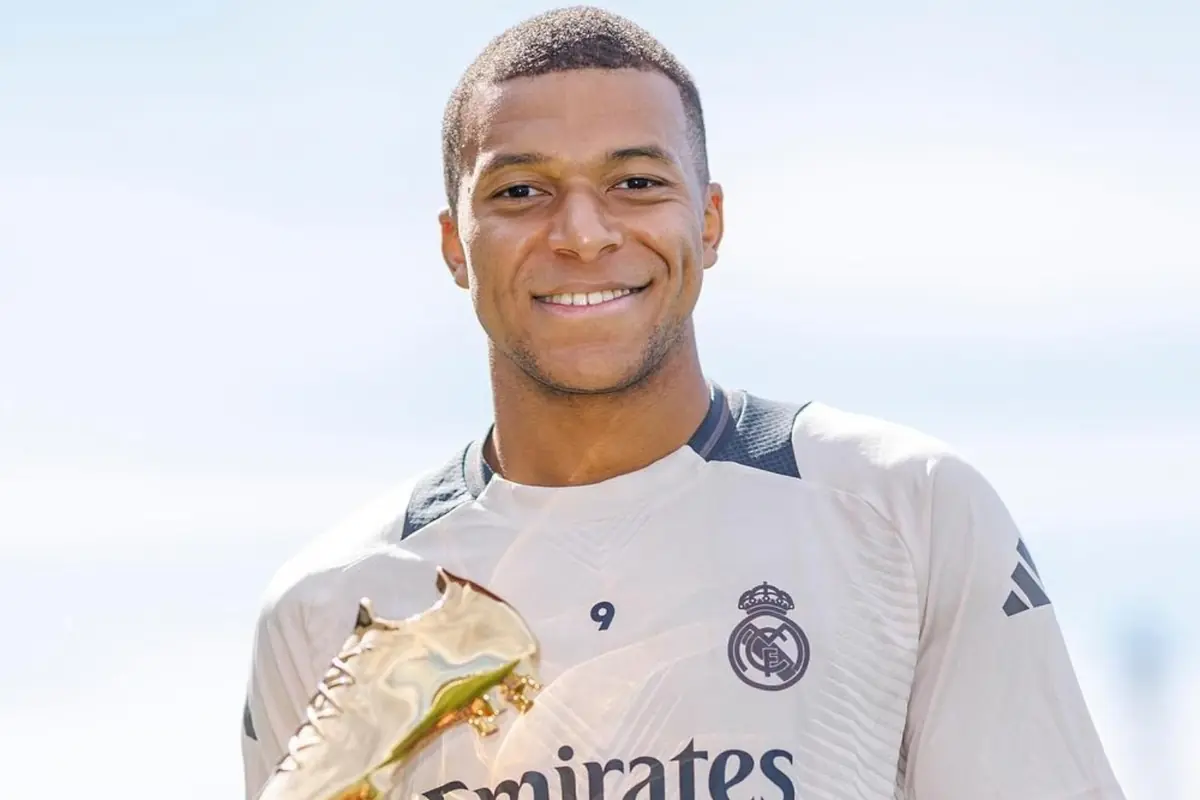 Futbolista con camiseta del Real Madrid sosteniendo un trofeo de bota dorada y sonriendo frente a un fondo claro
