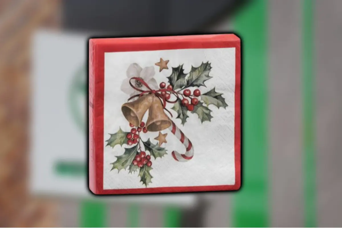Servilleta decorativa con borde rojo que tiene un diseño navideño de campanas doradas, hojas de acebo, frutos rojos, una estrella y un bastón de caramelo Servilleta decorativa con borde rojo que tiene un diseño navideño de campanas doradas, hojas de acebo, frutos rojos, una estrella y un bastón de caramelo
