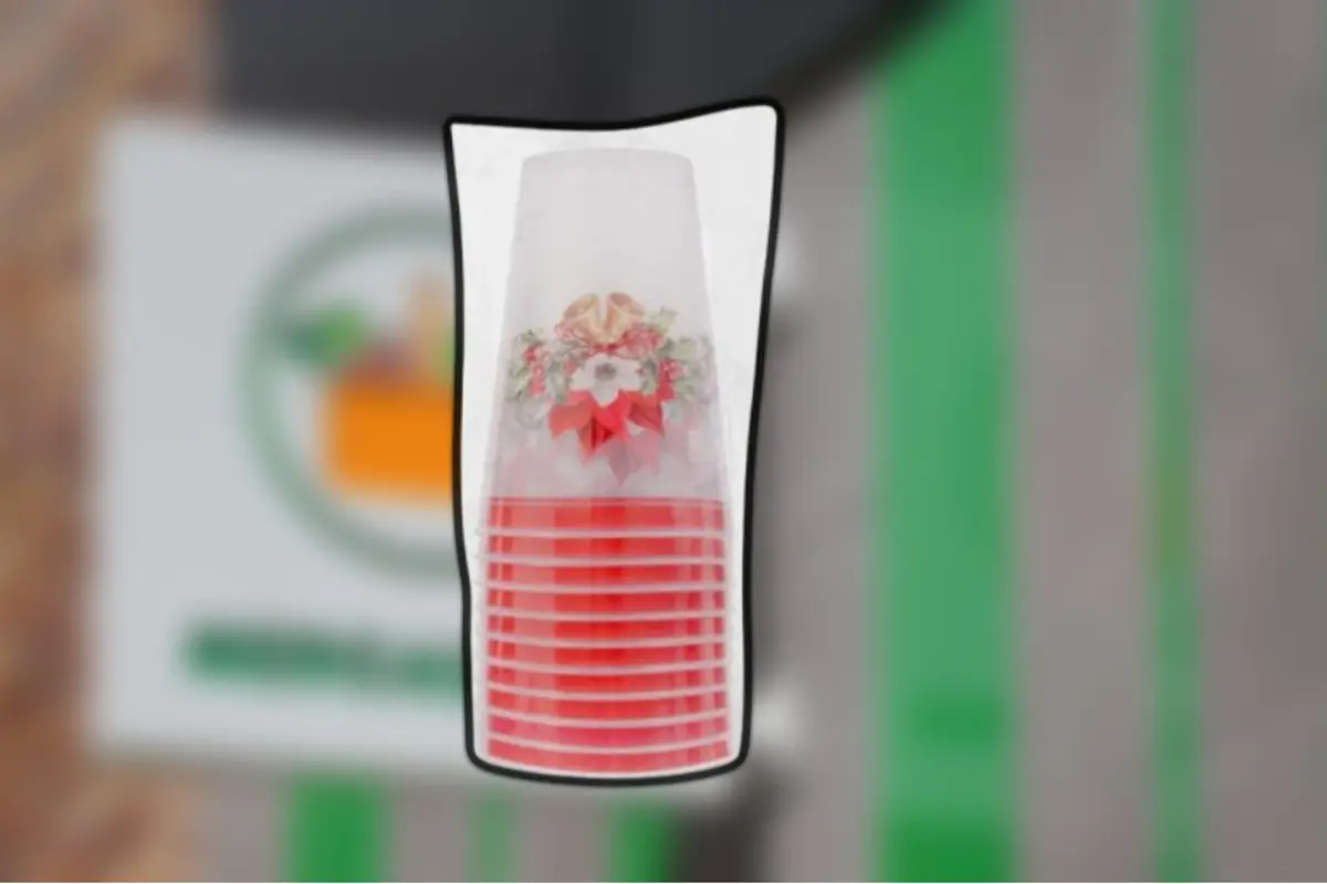 Vasos de plástico apilados con diseño navideño de flores y moño rojo sobre un fondo desenfocado.
