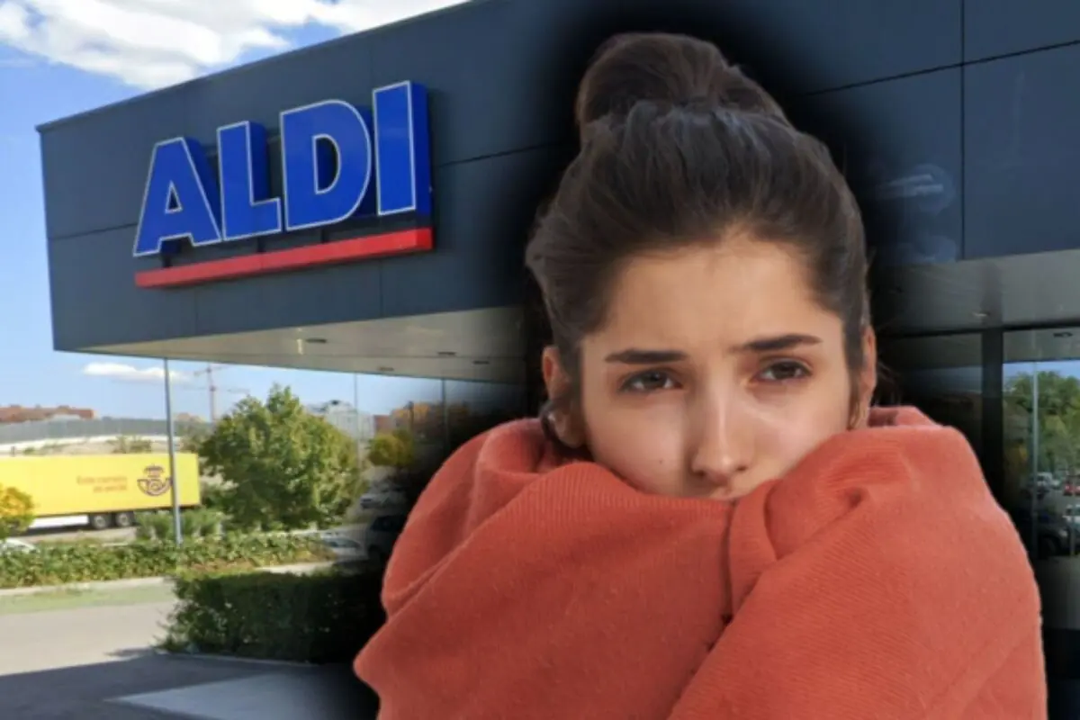 Una mujer con suéter naranja parece tener frío frente a una tienda ALDI.