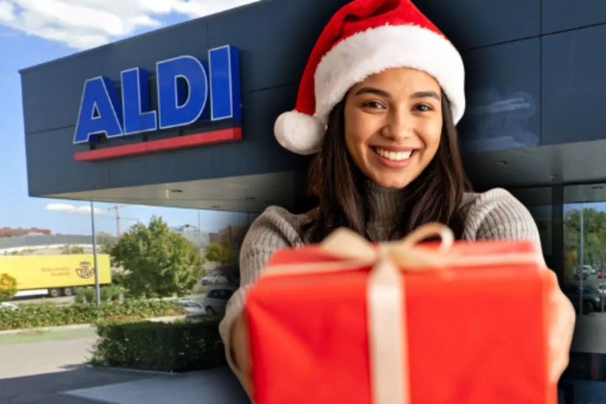 Mujer sonriente con gorro de Papá Noel ofreciendo un regalo envuelto en rojo frente a un supermercado Aldi.