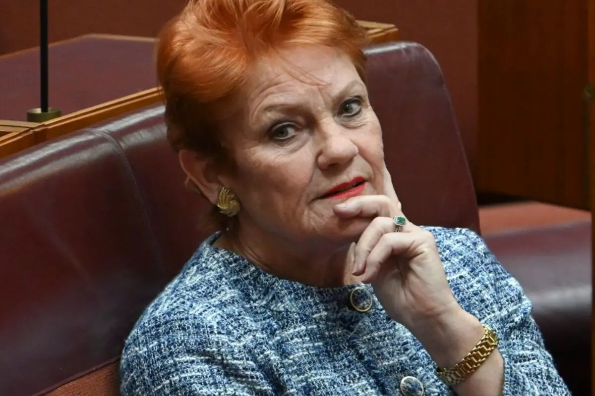 Mujer de cabello corto y rojizo sentada en una silla de cuero marrón con expresión pensativa y la mano en el rostro, lleva un saco azul y accesorios dorados.