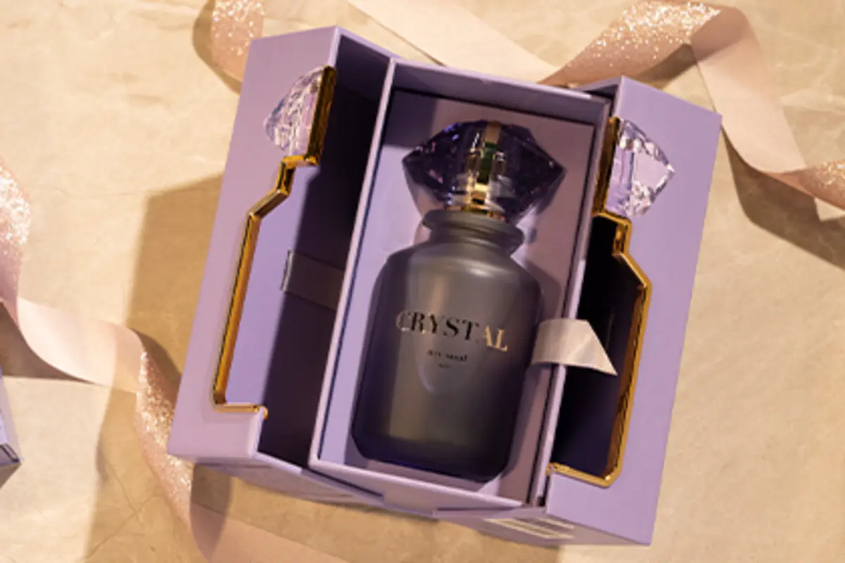 Caja lila abierta con frasco de perfume Crystal de vidrio mate y tapa en forma de diamante sobre fondo beige con lazo brillante