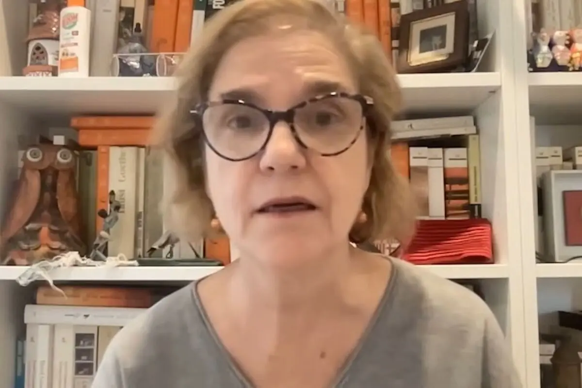 Dona de cabell curt i ulleres fosques davant d'una prestatgeria plena de llibres i objectes decoratius