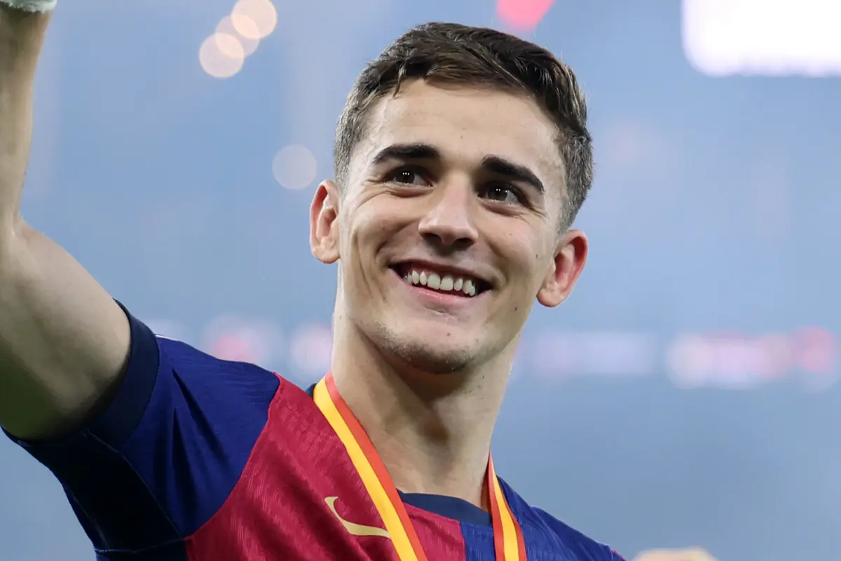 Jove futbolista somrient amb samarreta blava i vermella i medalla daurada penjada al coll en un estadi il·luminat