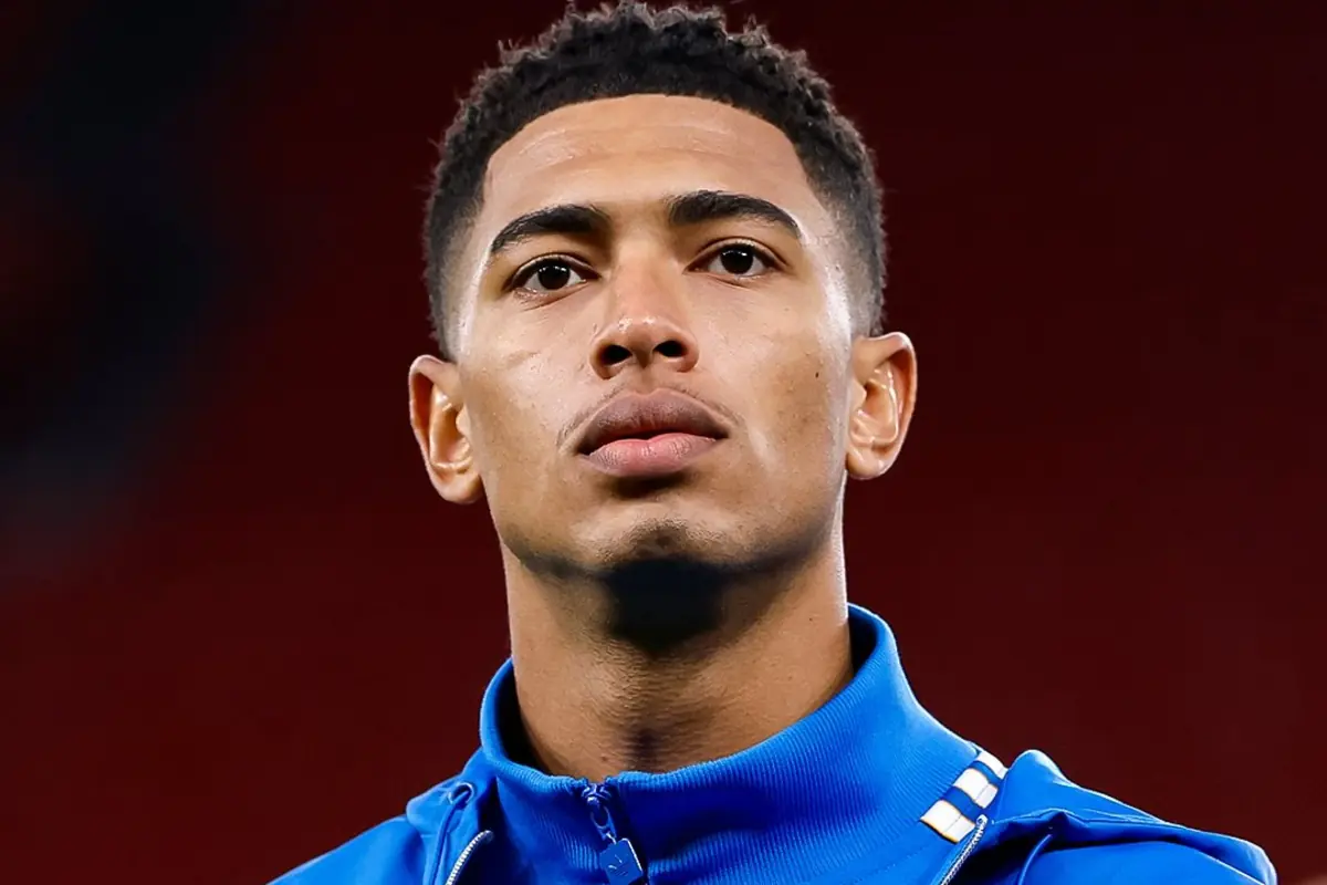 Jove amb jaqueta esportiva blava mirant cap al front amb expressió seriosa i fons fosc