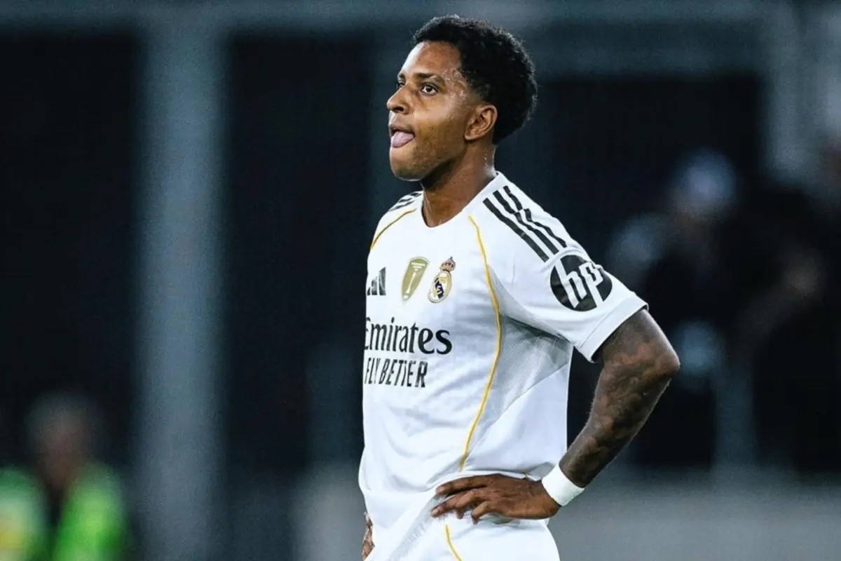 Soccer player in a white Real Madrid uniform on the field with hands on hips and a thoughtful expression