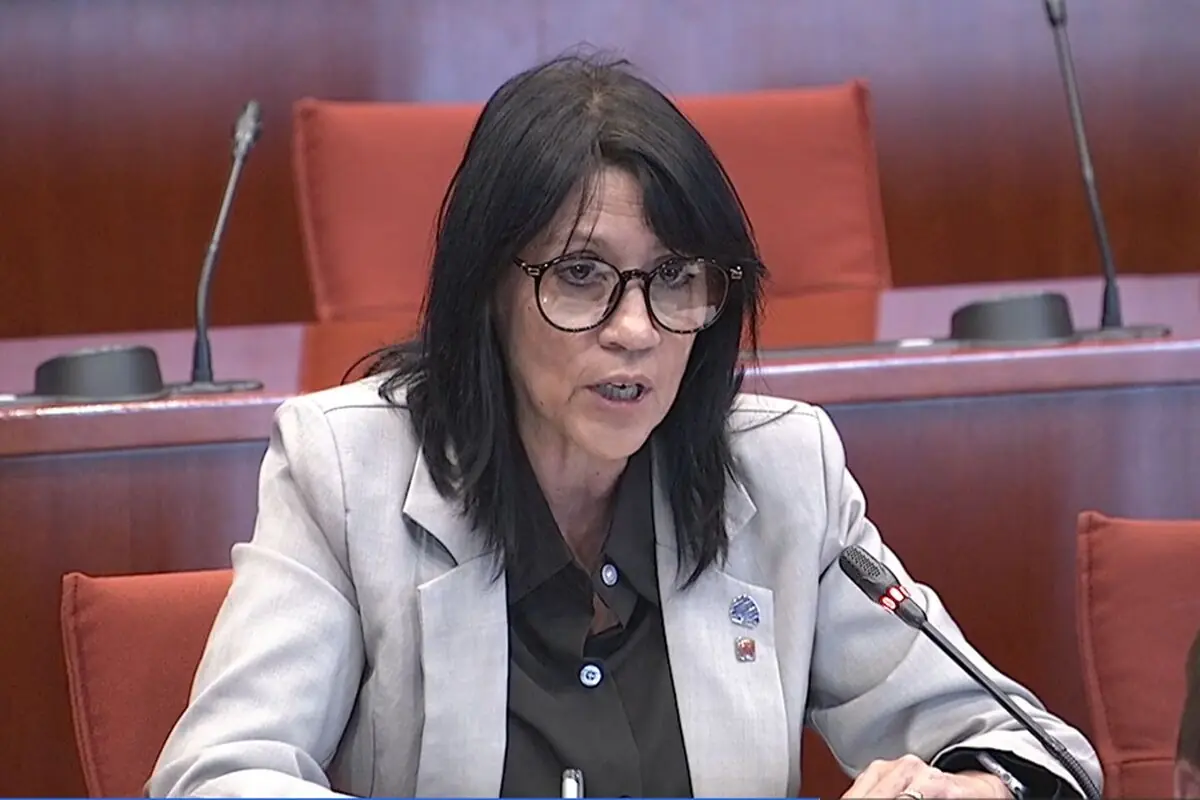 Dona de cabells foscos i ulleres parlant davant d’un micròfon en una sala de conferències amb seients vermells