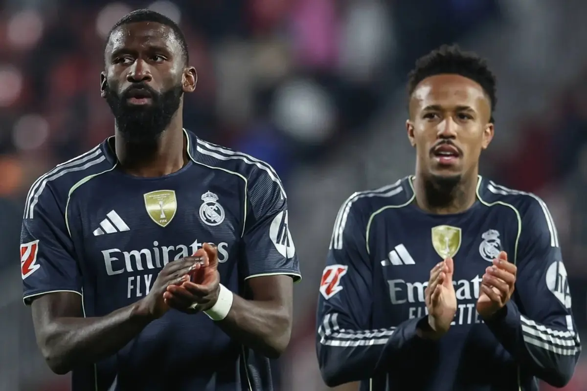 Two Real Madrid players applaud on the field wearing the navy blue away uniform.