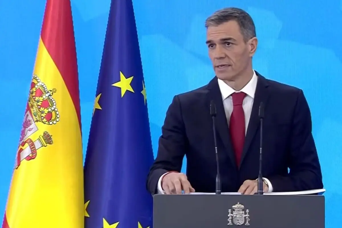 Hombre de traje y corbata roja hablando en un atril con las banderas de España y la Unión Europea de fondo