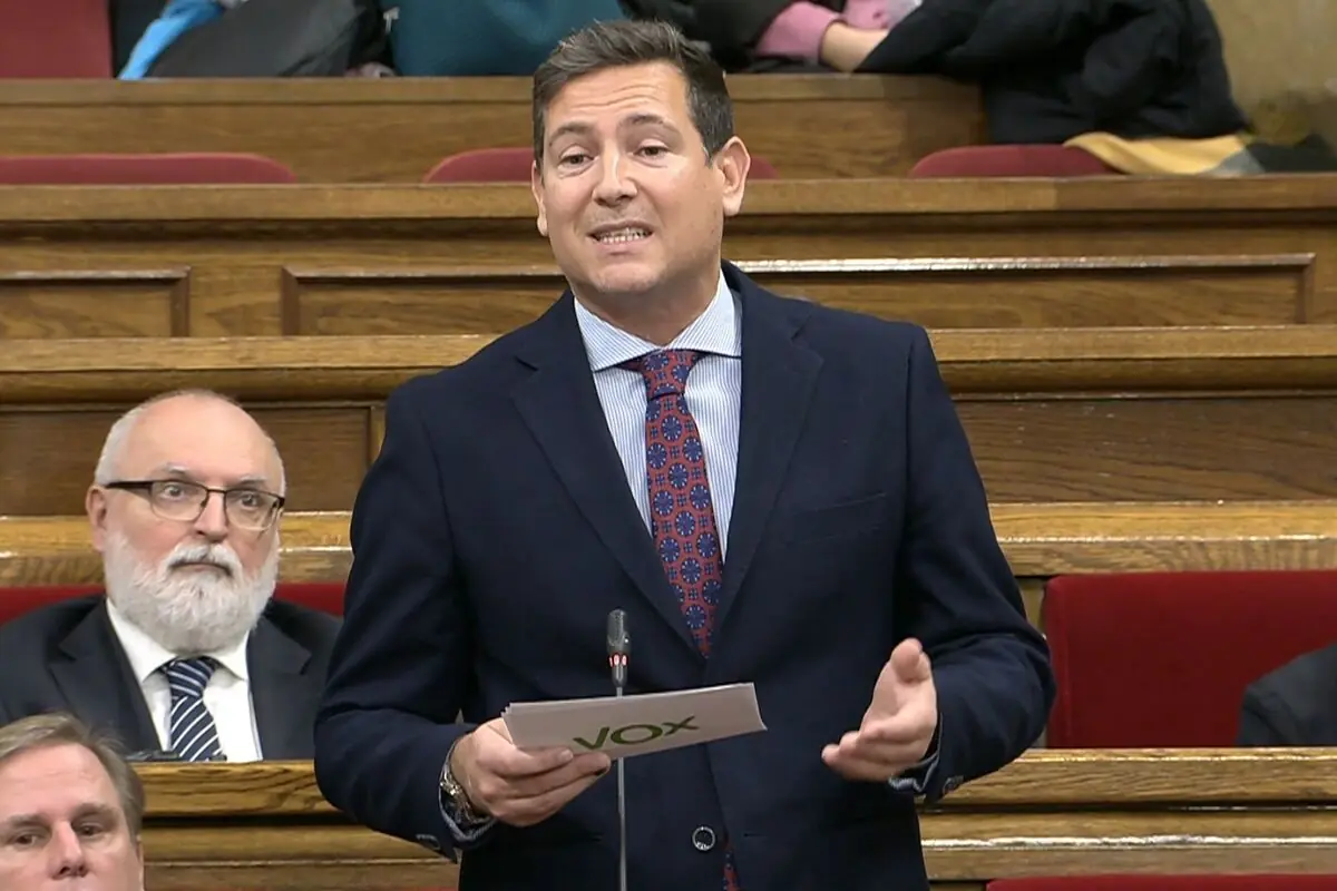 Hombre de traje hablando en un parlamento mientras sostiene unos papeles con el logo de Vox Hombre de traje hablando en un parlamento mientras sostiene unos papeles con el logo de Vox