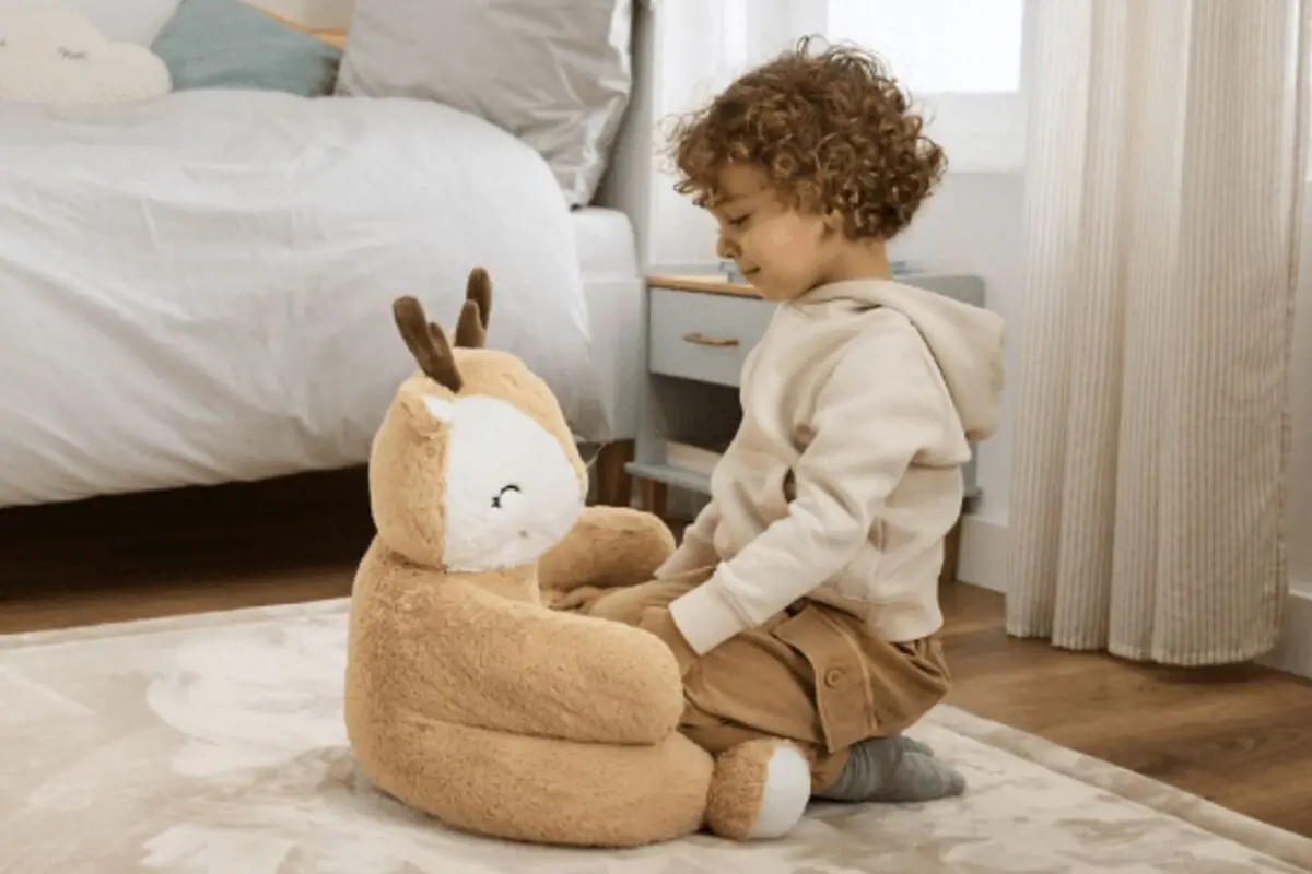 Niño pequeño sentado en el suelo de una habitación infantil jugando frente a un gran peluche con forma de ciervo de Aldi. Niño pequeño sentado en el suelo de una habitación infantil jugando frente a un gran peluche con forma de ciervo de Aldi.