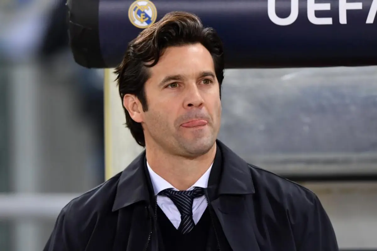 Hombre de cabello oscuro con traje y corbata mirando hacia el frente con el logo del Real Madrid y la palabra UEFA de fondo