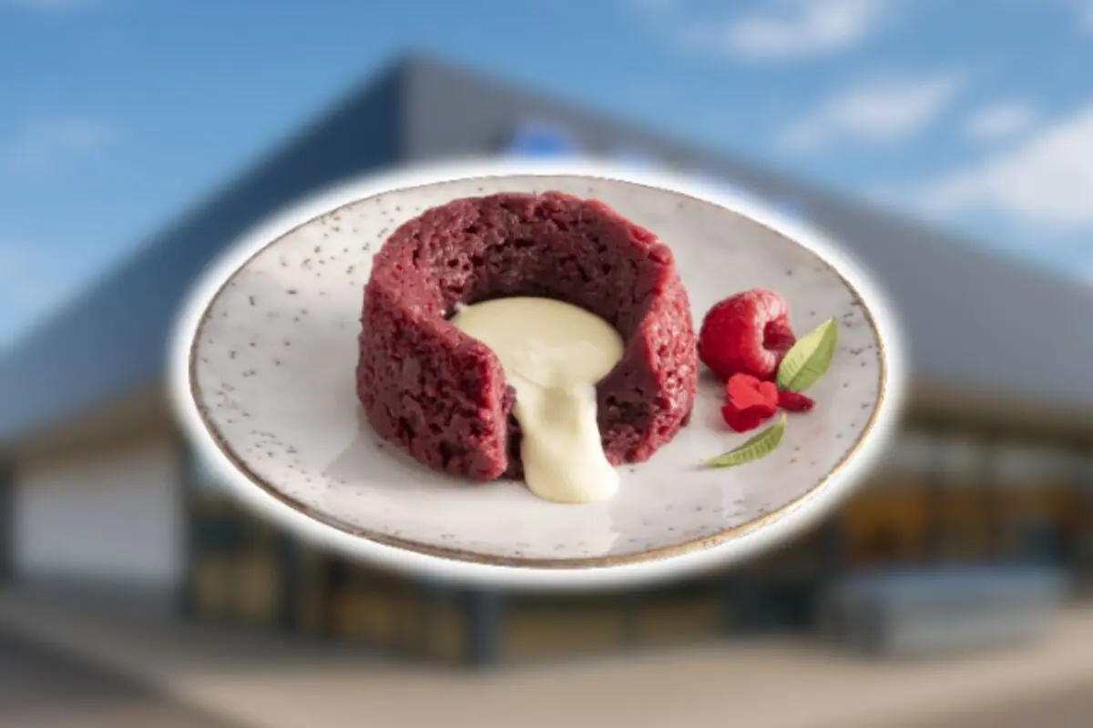 Postre tipo volcán de chocolate rojo con relleno cremoso blanco de Aldi acompañado de frambuesa y hojas verdes sobre un plato blanco.