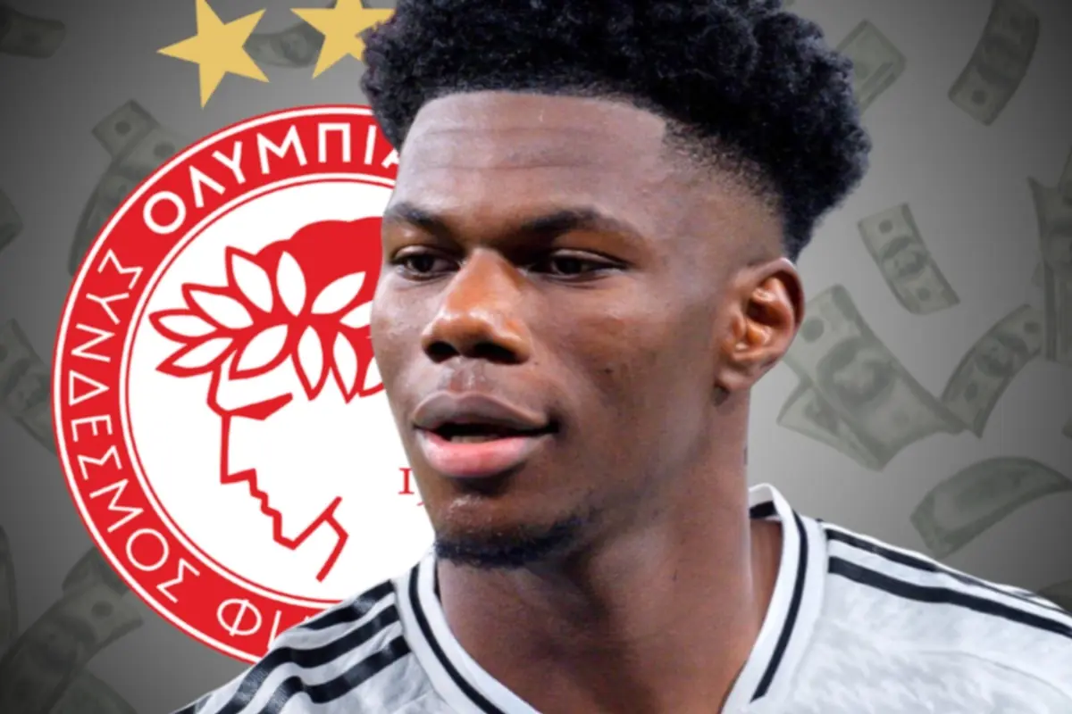 Soccer player wearing a black and white jersey in front of the Olympiacos crest with bills in the background