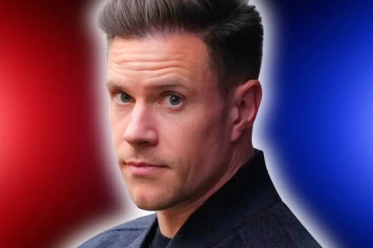 Retrat d’un home de cabell curt i fosc mirant seriós a la càmera amb un fons difuminat en tons vermells i blaus