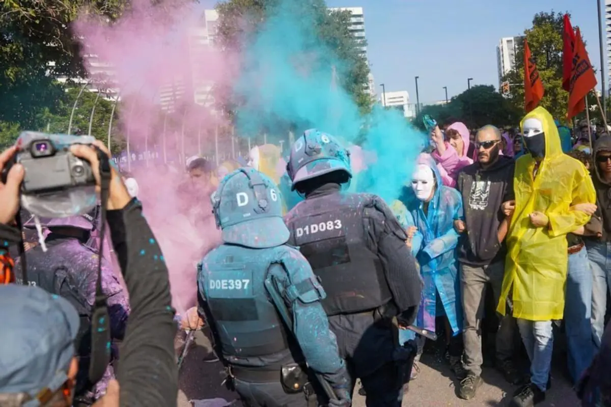 Policías antidisturbios enfrentan a manifestantes que lanzan polvos de colores mientras algunos llevan máscaras y capas de colores en una protesta urbana