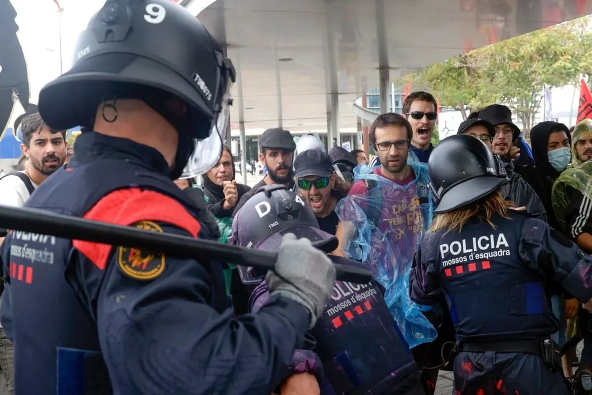 Policías antidisturbios enfrentándose a un grupo de manifestantes que gritan y muestran gestos de protesta en la calle.