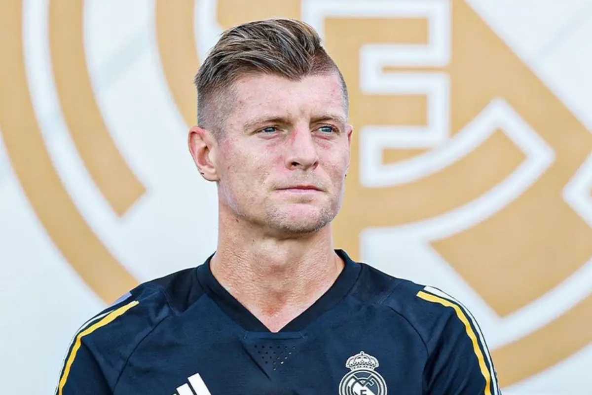 Futbolista con camiseta de entrenamiento del Real Madrid posando frente a un fondo con el escudo del club Futbolista con camiseta de entrenamiento del Real Madrid posando frente a un fondo con el escudo del club