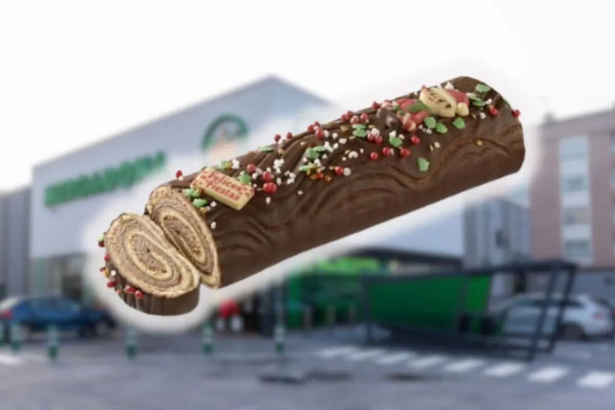 Tronco de Navidad de chocolate decorado con sprinkles de colores y mensaje de felices fiestas frente a un supermercado Mercadona desenfocado