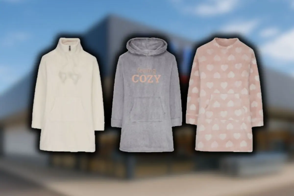 Tres batas de invierno en colores crema, gris y rosa de Aldi con corazones sobre un fondo desenfocado de una tienda de la cadena.