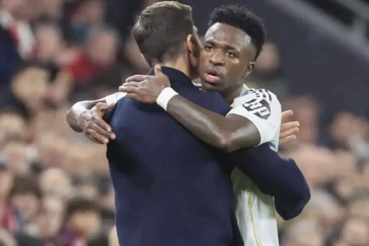 Dos futbolistes s’abracen al camp durant un partit, un d’ells mostra una expressió seriosa.