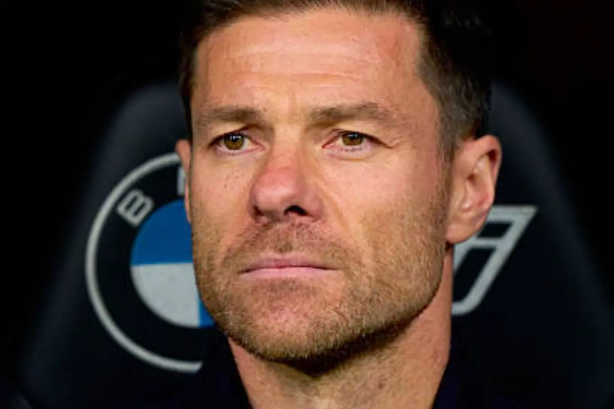 Home de cabell curt i barba retallada amb expressió seriosa assegut davant d’un respatller amb el logotip de BMW desenfocat al fons