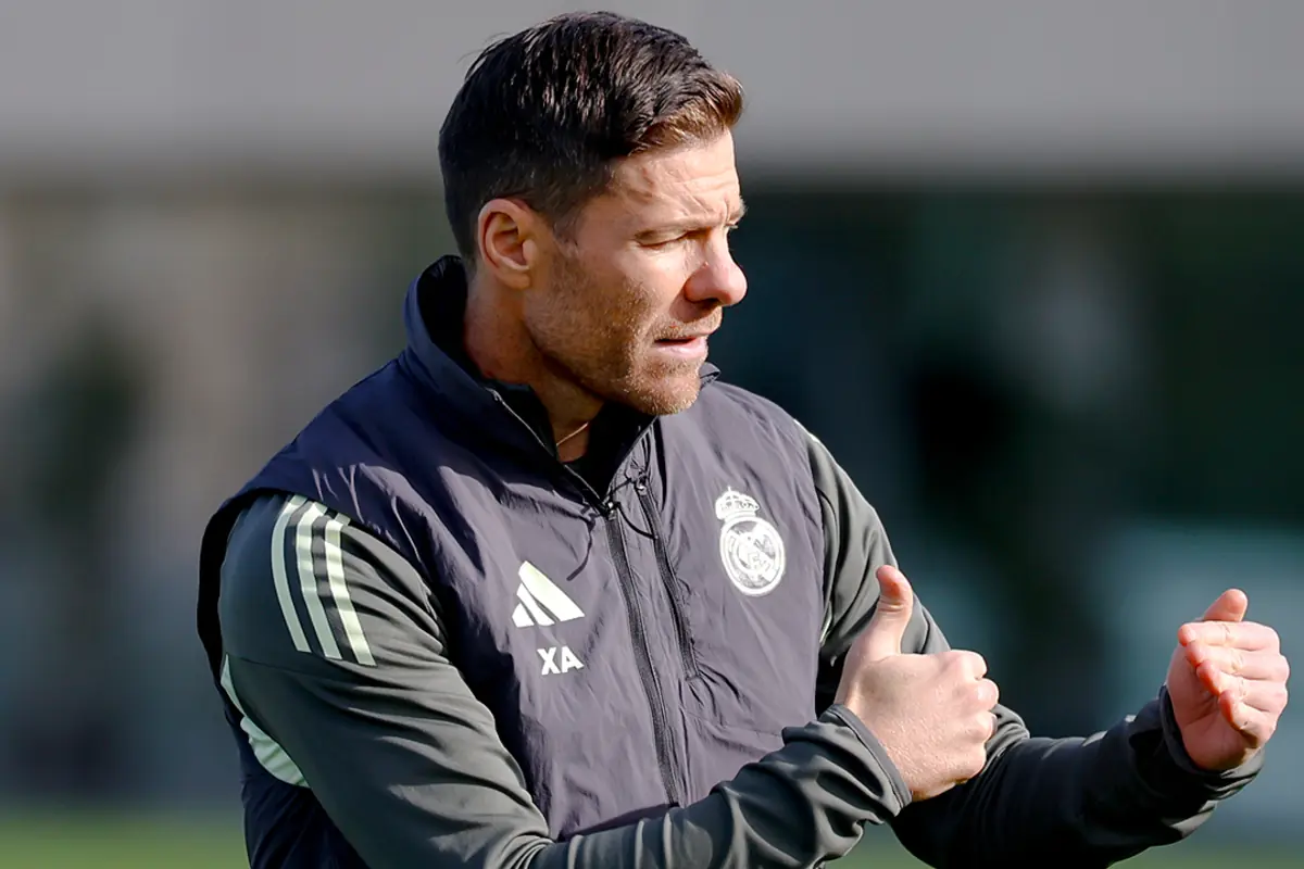 Entrenador de futbol amb jaqueta del Reial Madrid fent un gest amb les mans en un camp d’entrenament