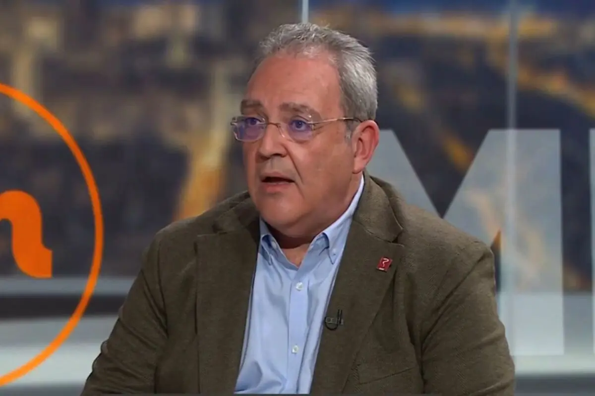 Home de cabells canosos i ulleres amb jaqueta marró i camisa blau clar parlant en un estudi de televisió