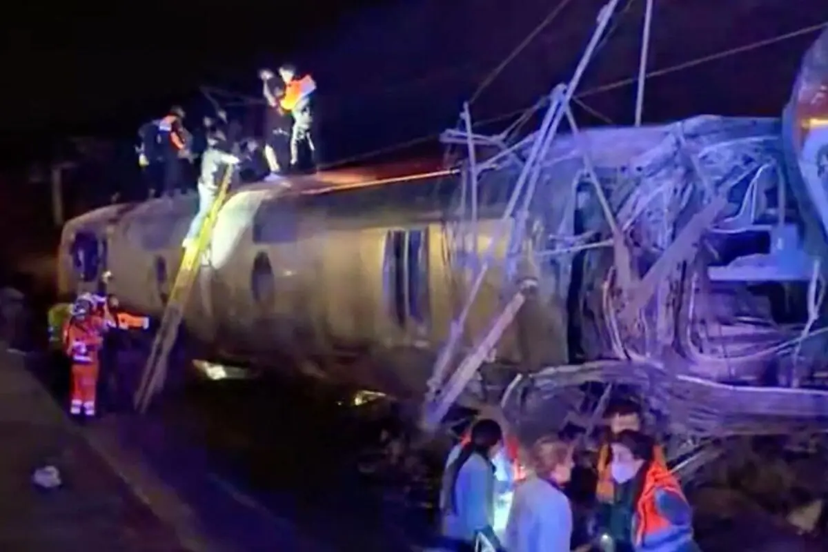 Els equips de rescat treballen de nit al costat d’un vagó de tren bolcat i destrossat després d’un accident ferroviari.