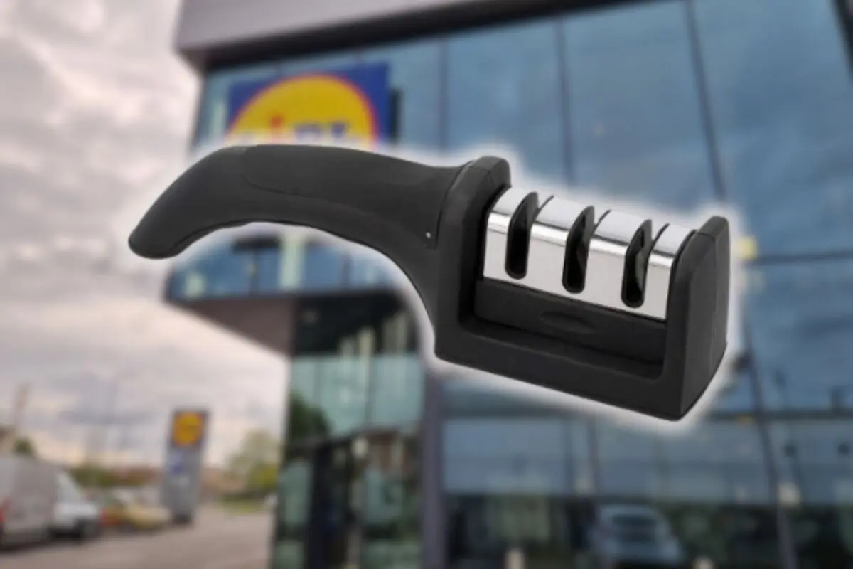 Afilador de cuchillos manual negro con tres ranuras metálicas en primer plano frente a la fachada de un supermercado Lidl desenfocado
