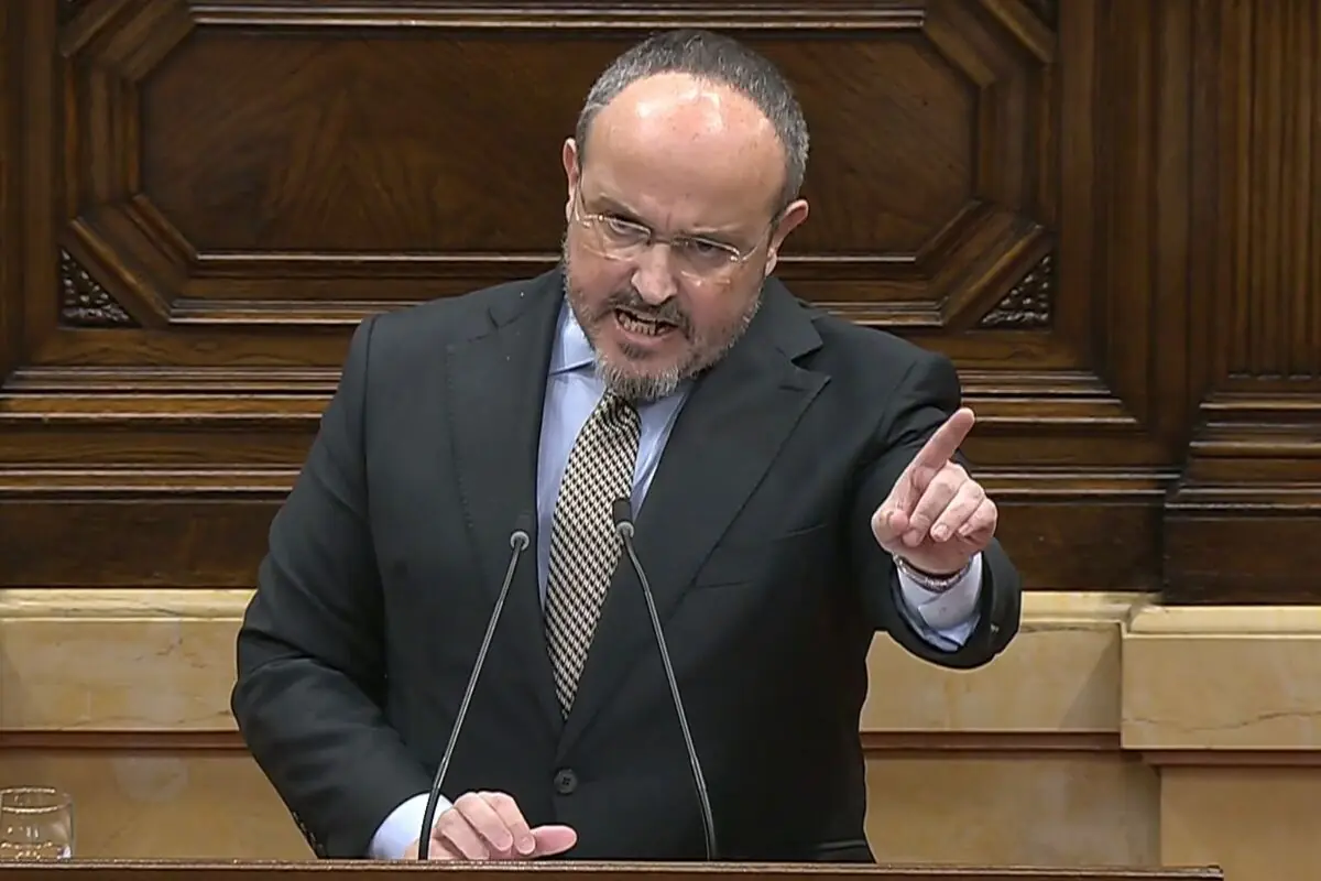 Hombre de mediana edad con traje oscuro y corbata hablando en un atril de madera y señalando con el dedo índice durante un discurso en un parlamento