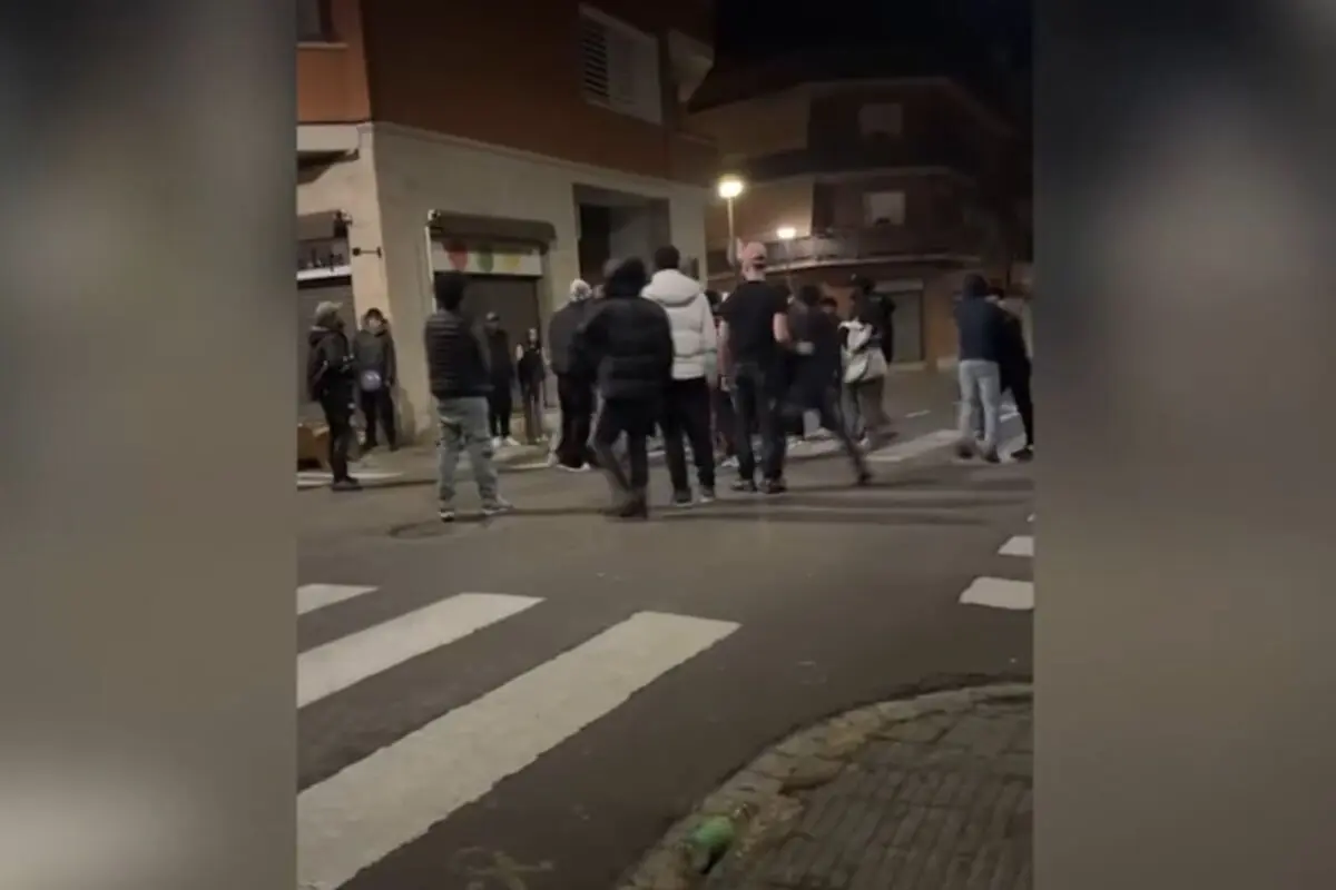 Grup de persones reunides de nit en una cantonada d’un carrer urbà amb passos de vianants i edificis residencials de fons