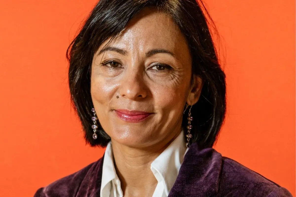 Retrat d’una dona de mitjana edat amb cabell curt i fosc somrient lleument davant d’un fons taronja brillant