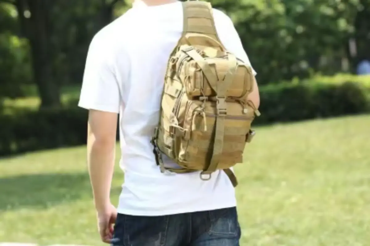 Persona de espaldas con camiseta blanca y mochila táctica color caqui cruzada al hombro en un parque verde Persona de espaldas con camiseta blanca y mochila táctica color caqui cruzada al hombro en un parque verde