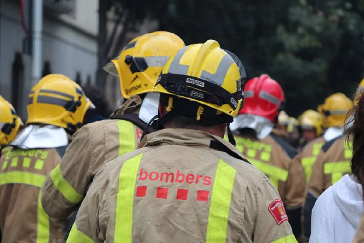Grup de bombers amb cascos grocs i vermells vistos des de darrere durant un operatiu al carrer