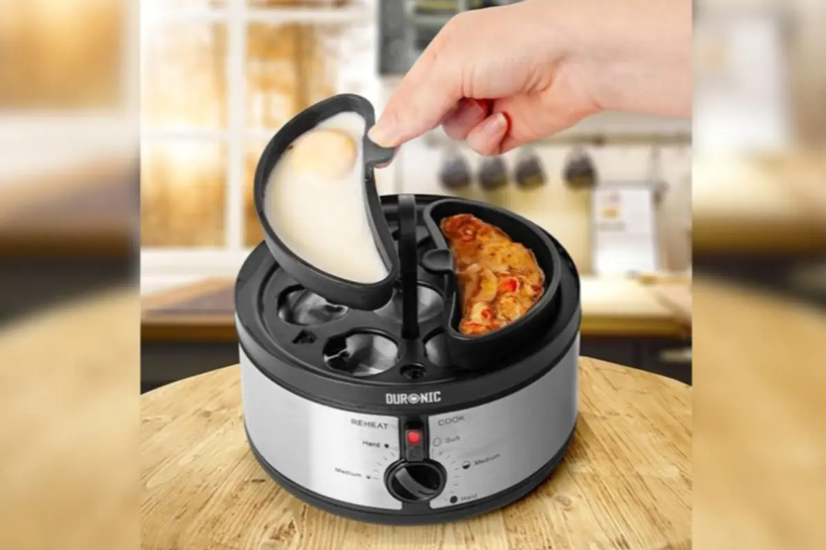 Mano levantando la tapa de una máquina eléctrica para cocinar huevos y preparar desayuno sobre una mesa de madera en una cocina