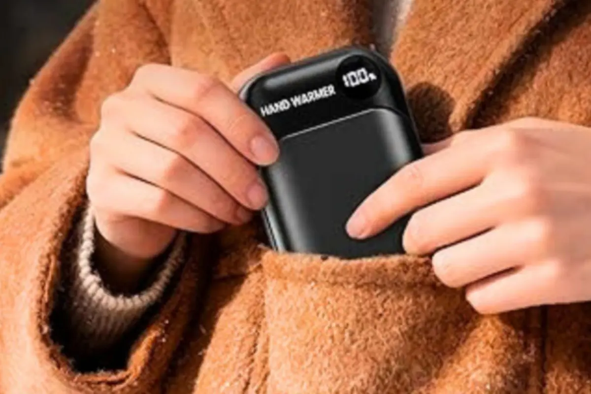 Persona guardando un calentador de manos negro con pantalla digital en el bolsillo de un abrigo de invierno marrón