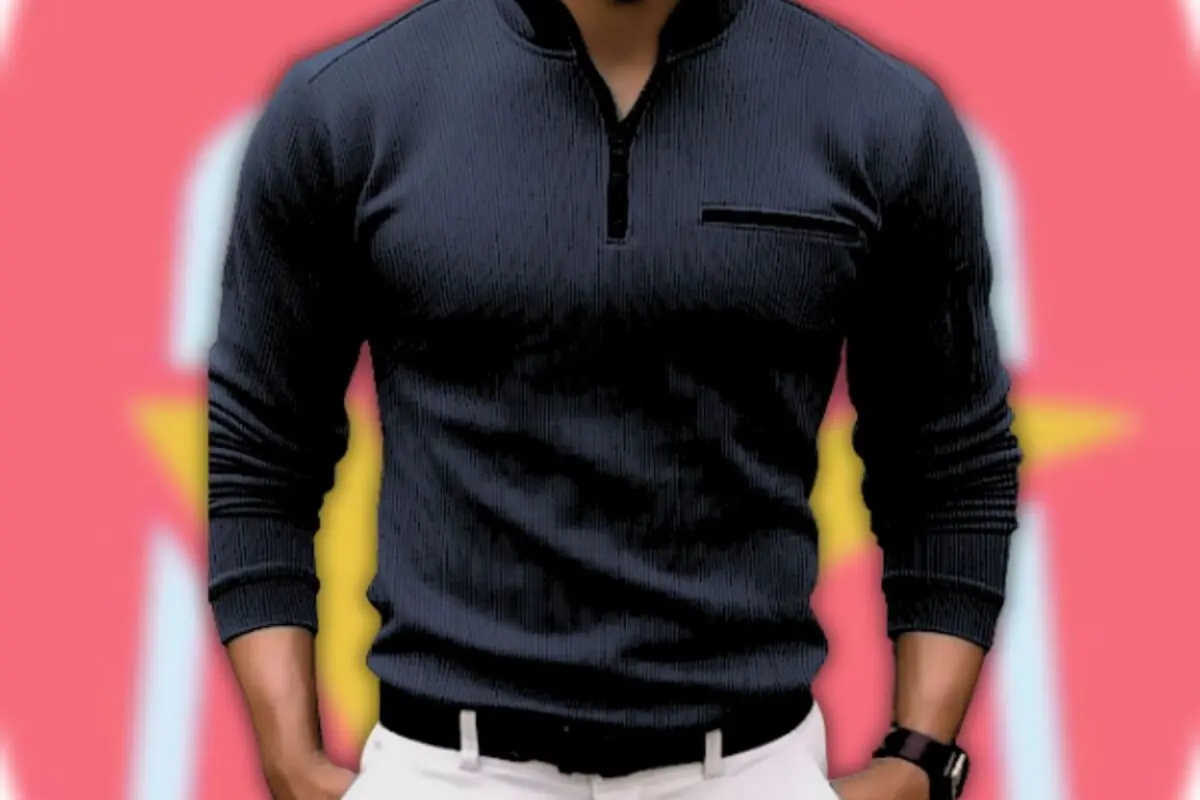 Hombre vistiendo suéter negro de manga larga con cremallera corta y pantalones blancos sobre fondo rosa con formas amarillas desenfocadas