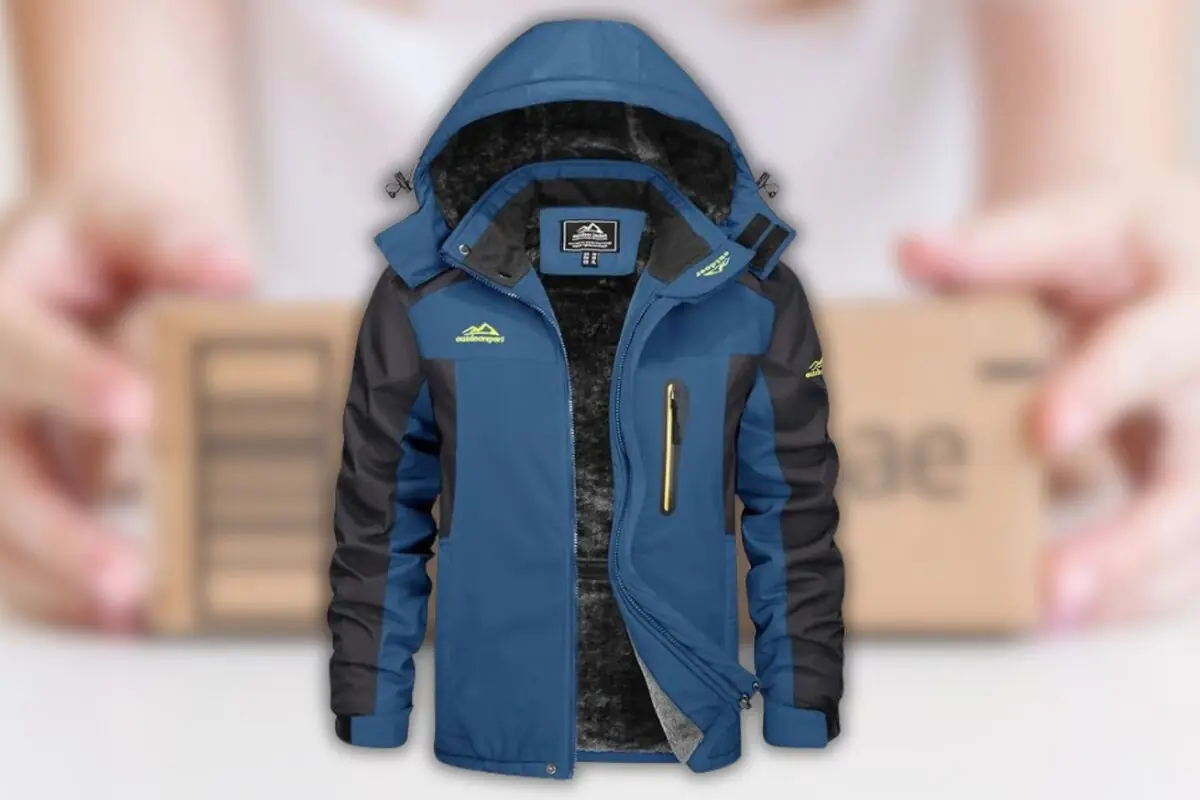 Chaqueta azul y negra con capucha y forro interior de peluche sobre fondo desenfocado de manos sosteniendo una caja de cartón