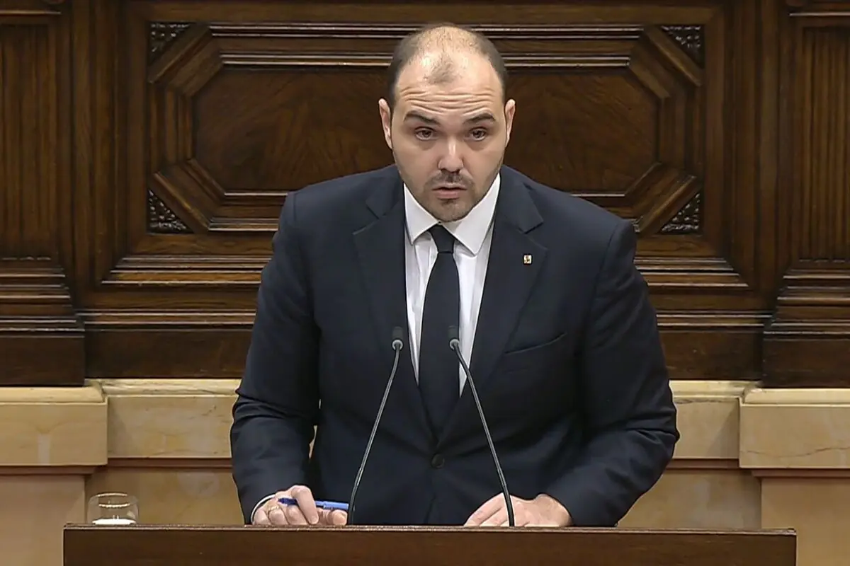 Hombre con traje oscuro hablando en un atril de madera con dos micrófonos en un parlamento