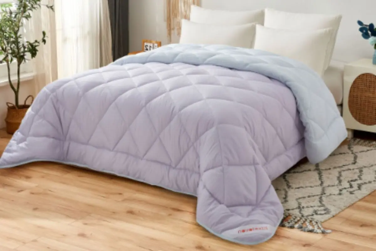 Cama matrimonial con edredón acolchado lila y manta celeste en dormitorio moderno con piso de madera