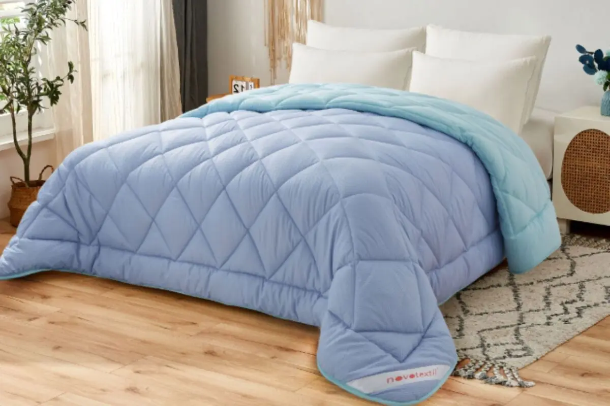 Cama matrimonial con edredón acolchado azul claro en dormitorio moderno con cojines blancos y suelo de madera