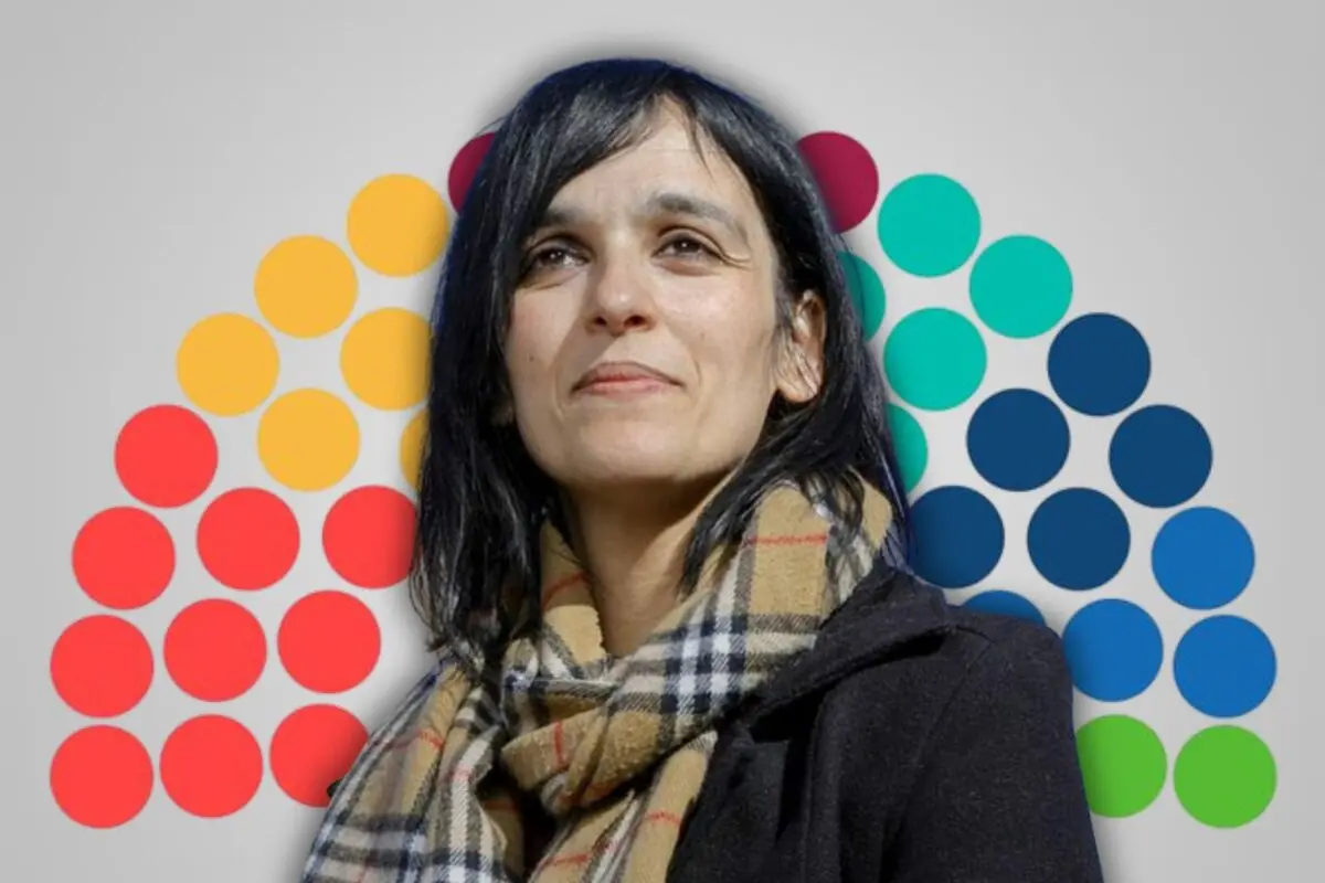 Mujer de cabello oscuro con bufanda de cuadros y abrigo negro posando frente a un fondo gris con semicírculo de puntos de colores