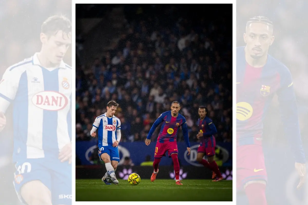 Partit de futbol entre jugadors de l’Espanyol i del Barcelona disputant la pilota al camp amb el públic de fons