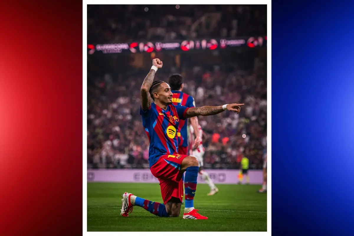 Futbolista del FC Barcelona agenollat a la gespa celebrant un gol i assenyalant cap a la graderia durant un partit nocturn en un estadi ple