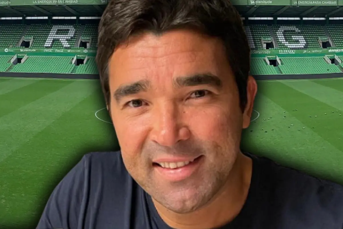Primer plano de un hombre sonriente con camiseta oscura sobre un fondo de estadio de fútbol con gradas verdes