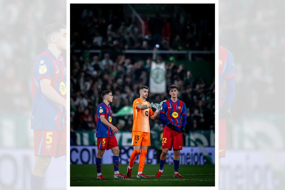 Tres jugadors del FC Barcelona amb uniforme blau i vermell conversen al camp durant un partit nocturn amb la graderia plena d’aficionats al fons