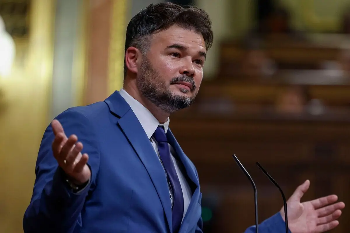 Home amb vestit blau parlant en un faristol amb els braços oberts en un saló parlamentari