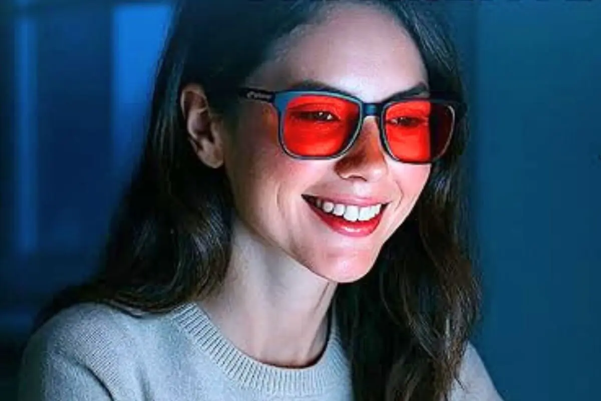 Mujer joven sonriendo mientras usa gafas con lentes rojos frente a una pantalla en un entorno oscuro Mujer joven sonriendo mientras usa gafas con lentes rojos frente a una pantalla en un entorno oscuro
